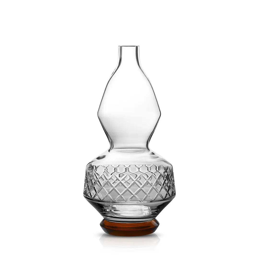 A close-up of the Majesty Flacon, a sculpted crystal decanter with deep angular cuts, an amber base, and a distinctive silhouette against a white background.
