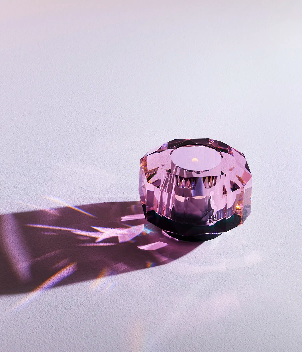 Pink crystal Texas Supreme Rose Tealight Holder lit with a candle, casting prismatic shadows and light reflections on a soft surface.